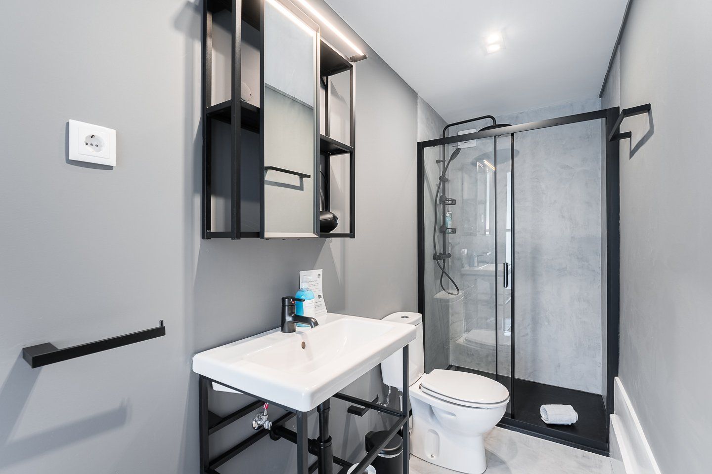Un baño moderno con un lavamanos blanco, un inodoro y una ducha con mampara de vidrio.