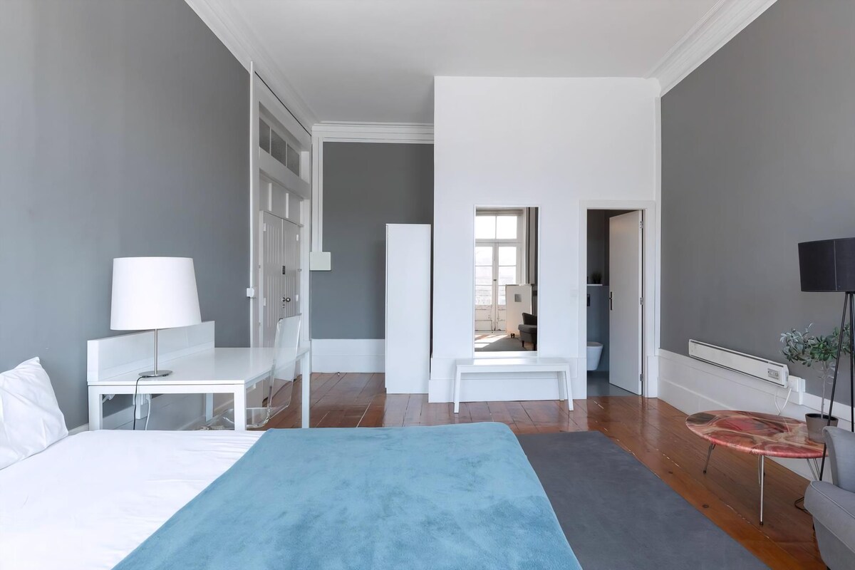Ein modernes Hotelzimmer mit Bett, Nachttisch, Lampe und Blick auf den Flur.