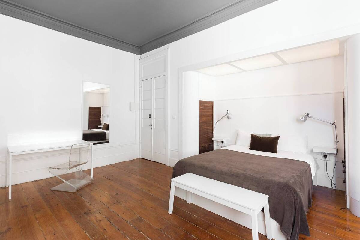 Une chambre à coucher moderne avec un grand lit, une table de chevet, un banc, un miroir et une armoire.