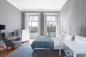 Une chambre d’hôtel moderne, équipée d’un lit, d’un bureau, d’une chaise et offrant une vue sur la ville grâce à de grandes fenêtres.