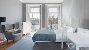 A modern bedroom with a bed, a desk, a chair, and a view of a cityscape through large windows. - Guestready - Innvict Residences (Porto)