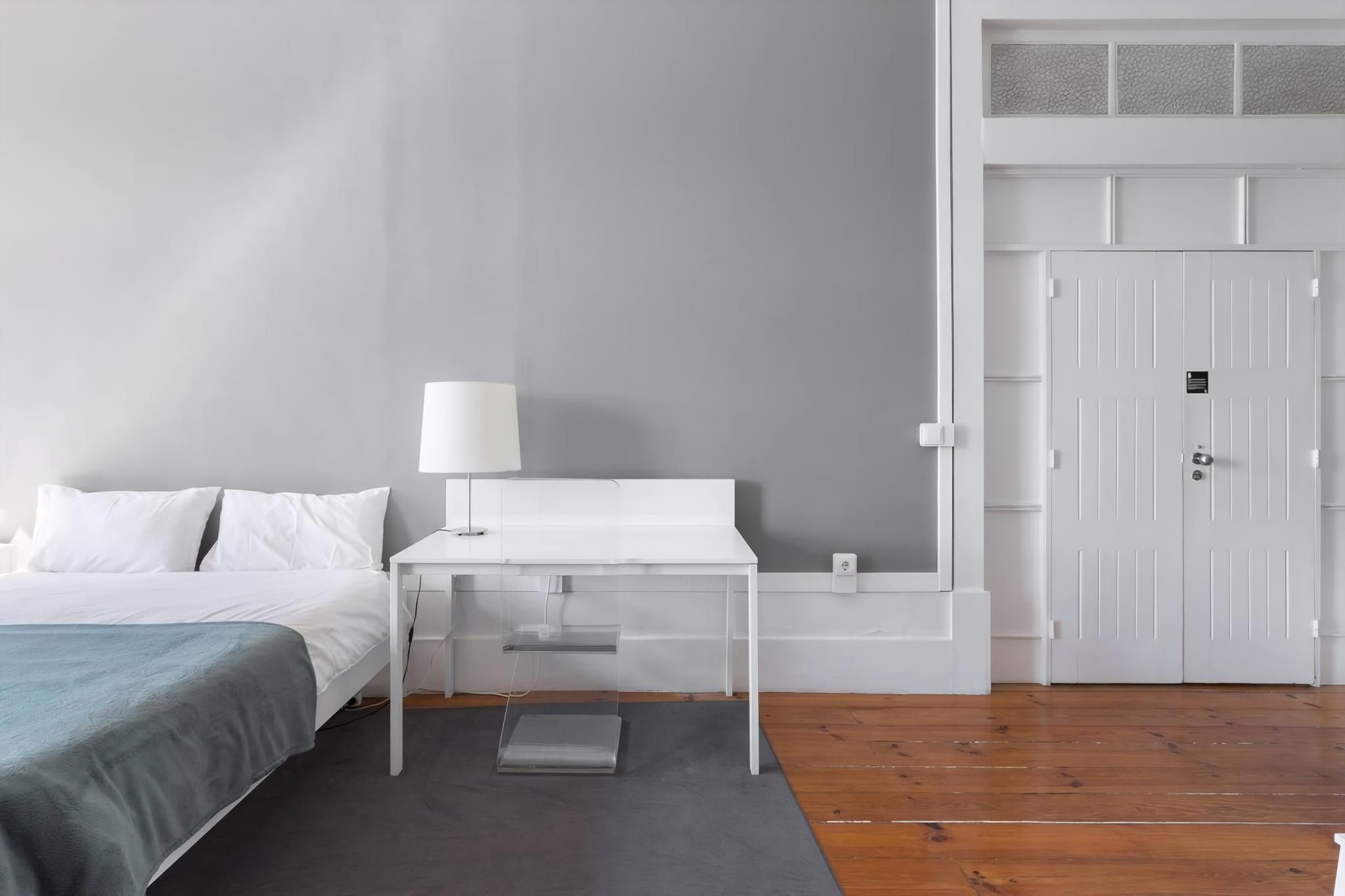 A hotel room with a bed, a desk, a chair, a nightstand, a lamp, and a wardrobe.