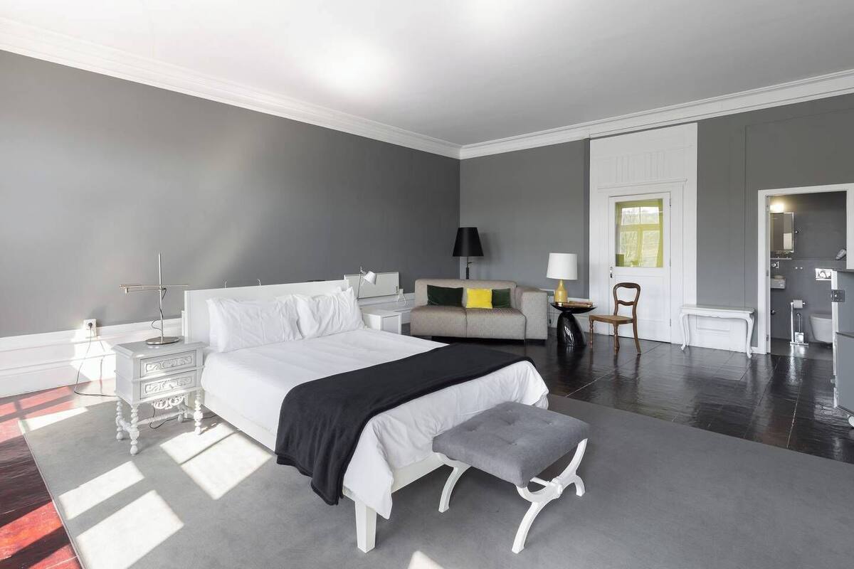 Une chambre d’hôtel moderne, dotée d’un grand lit, de tables de chevet, d’un canapé, d’une petite table avec une lampe et d’une salle de bain visible à travers une porte ouverte.
