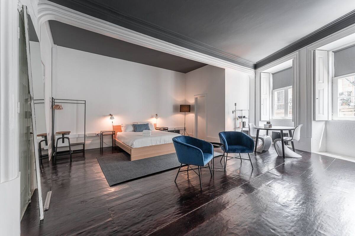 Une chambre d’hôtel moderne avec un grand lit, deux chaises bleues, une petite table et un bureau.