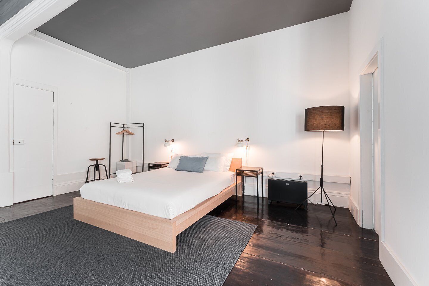 A modern bedroom with a wooden bed, bedside tables, a floor lamp, and a radiator.