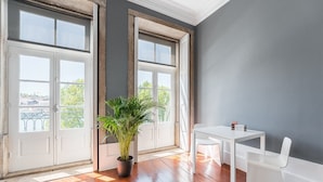 A room with a large window, a potted plant, a white table, and white chairs. - Guestready - Innvict Residences (Porto)