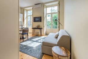 Un salon moderne avec un canapé, une petite table, un fauteuil et un téléviseur fixé au mur.