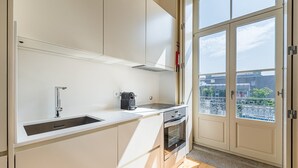 Une cuisine moderne avec des meubles blancs, un évier en acier inoxydable, une machine à café et un four.