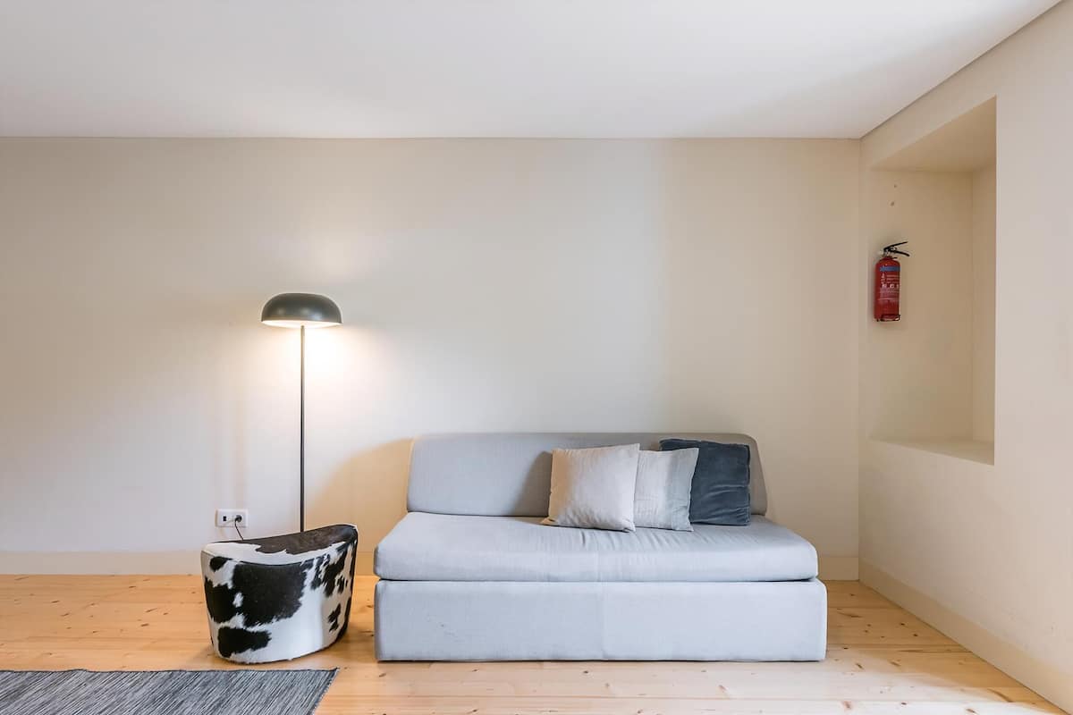 Een minimalistische woonkamer met een bank, een bijzettafeltje, een vloerlamp en een brandblusser.
