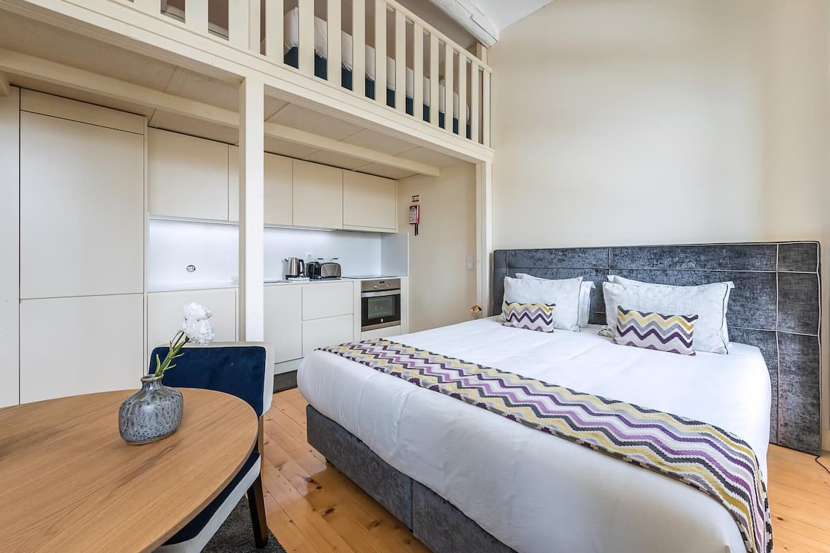 Een hotelkamer met een bed, een eettafel, een keukenhoek en een balkon.