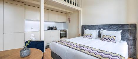 A hotel room with a bed, a dining table, a kitchen area, and a balcony.