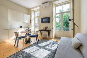 Un salón moderno con sofá, una mesa de comedor con sillas, televisor y un ventanal con vista a follaje.