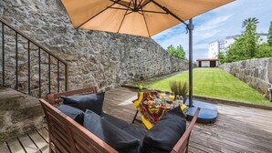 Une terrasse en bois avec un muret en pierre, un coin salon avec des coussins et une table préparée pour le petit-déjeuner.