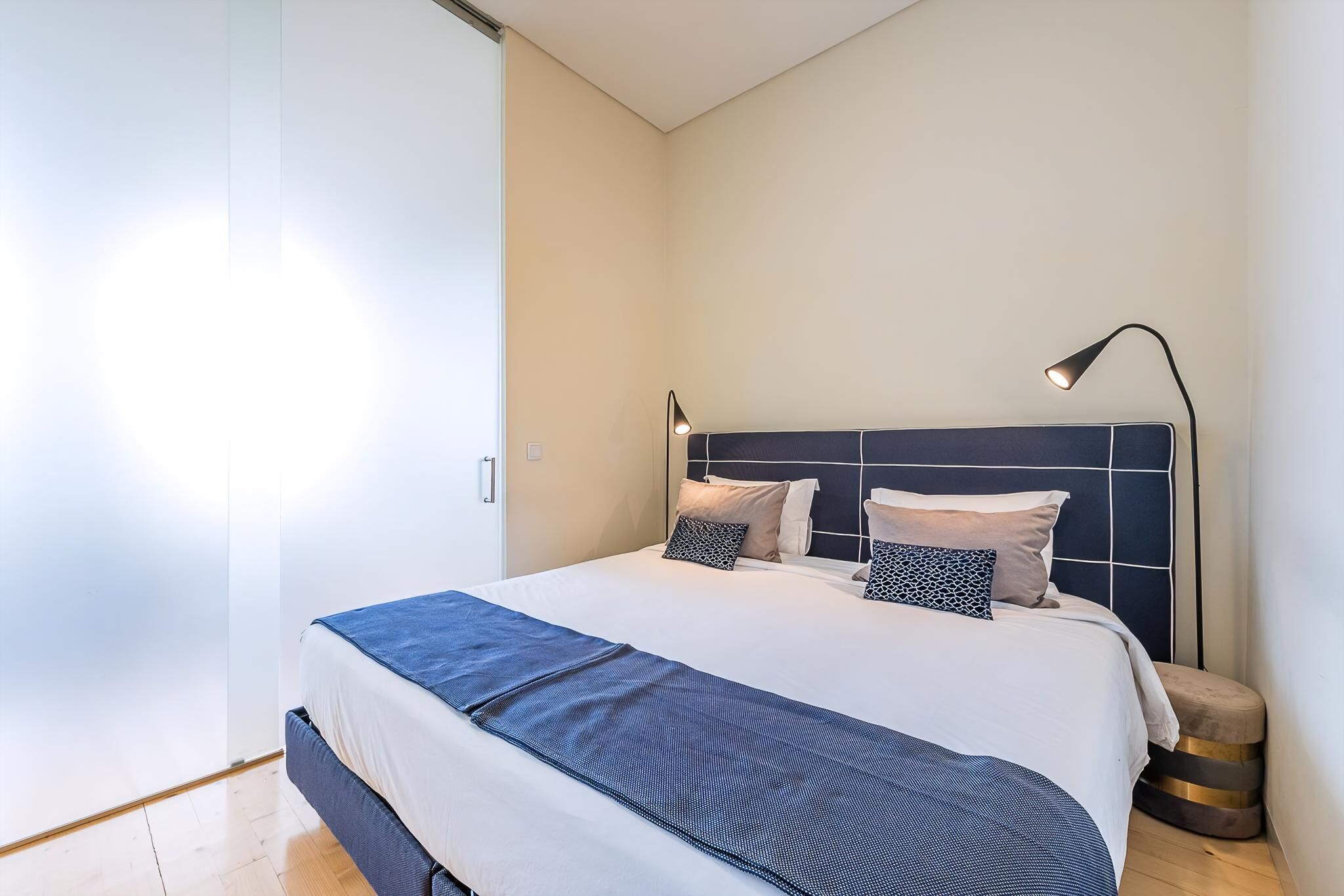 Une chambre à coucher moderne avec un lit, une lampe de chevet et un petit tabouret.