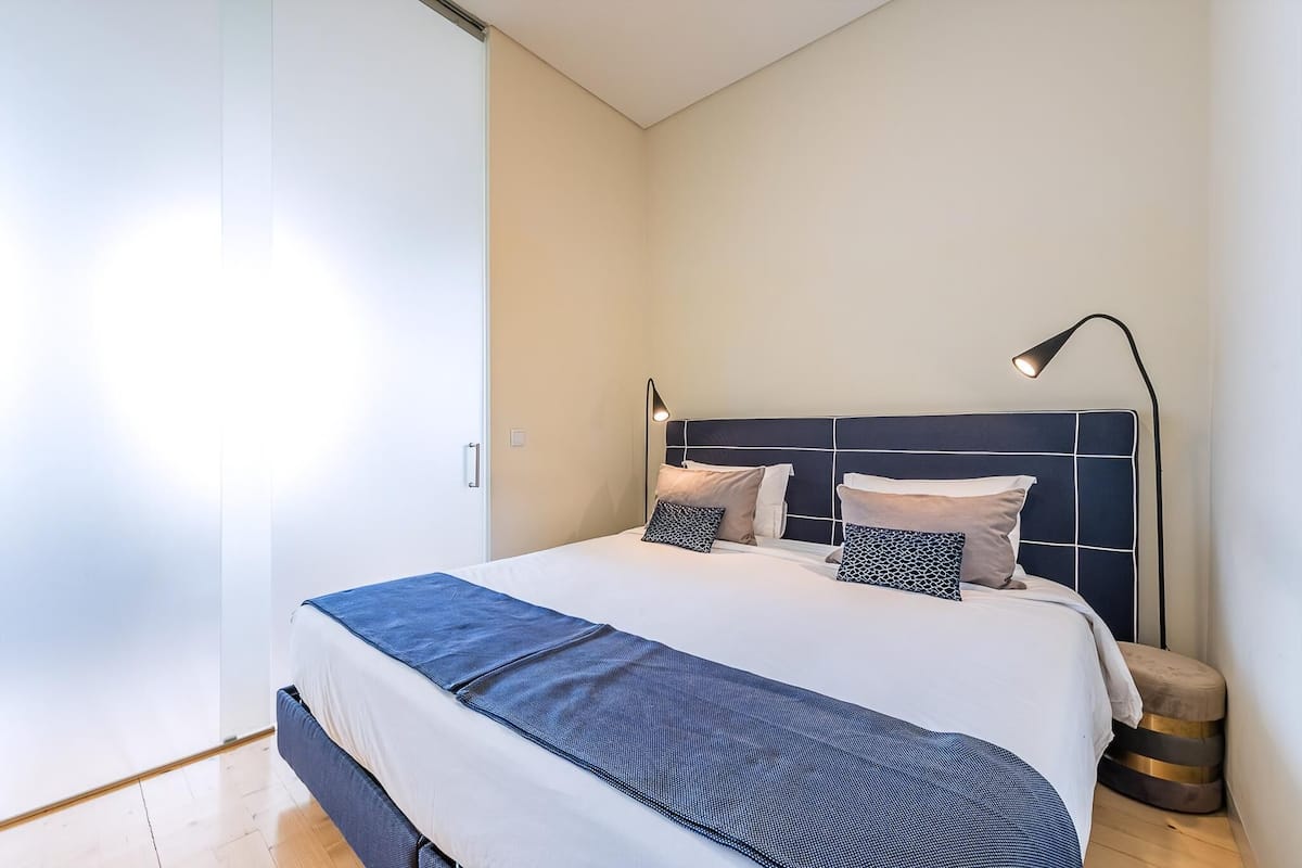 Een moderne slaapkamer met een bed, een bedlampje en een klein krukje.