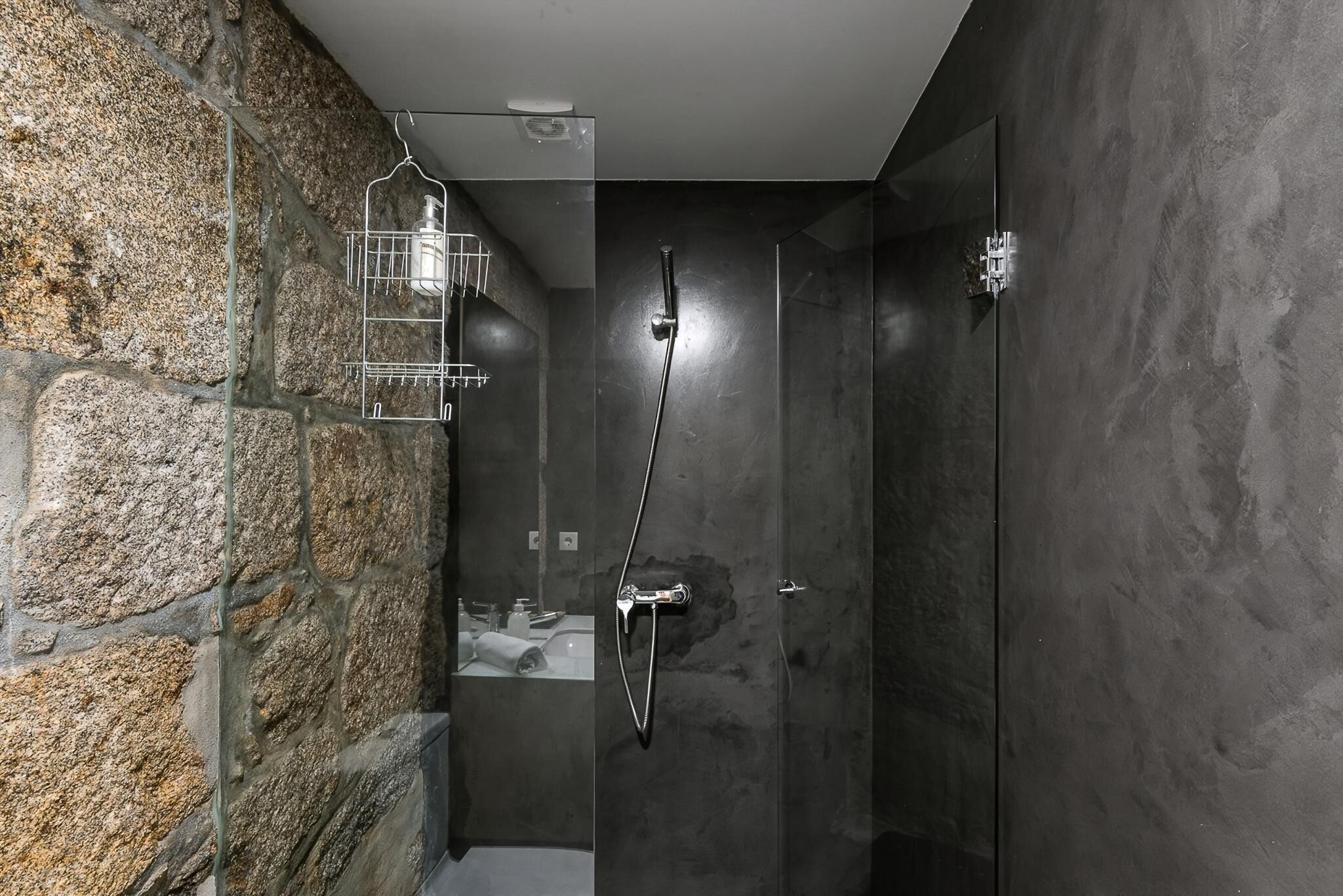 Una ducha moderna con puerta de vidrio, pared de piedra y estante de metal.