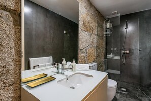 A modern bathroom with a granite wall, a white sink, a toilet, and a glass-enclosed shower. - Guestready - La Maison Aires Gouveia (Porto)