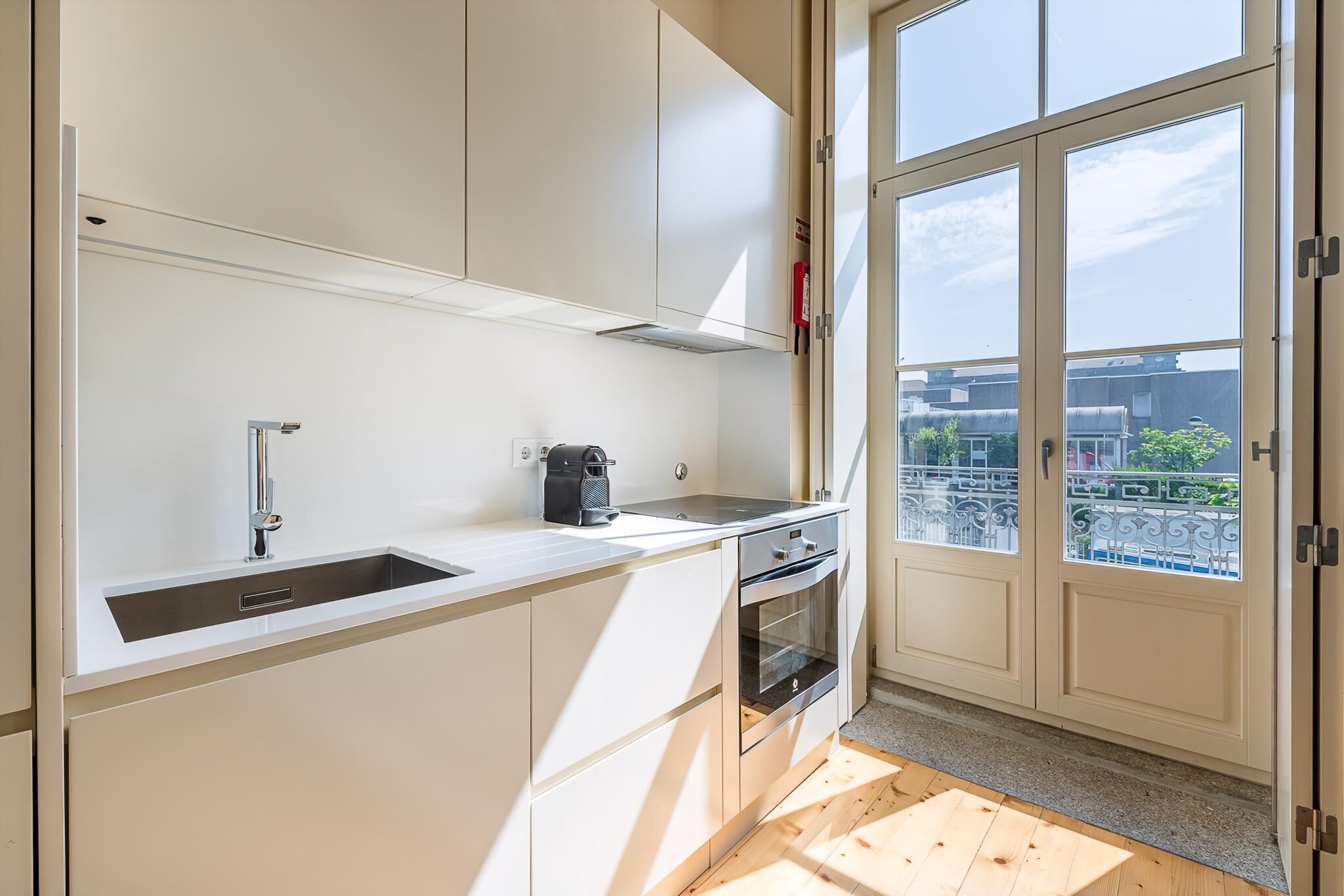Ett modernt kök med vita skåp, en diskho i rostfritt stål, en kaffebryggare och en ugn.