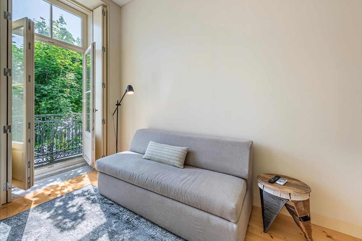 Een kamer met een bank, een kleine tafel, een lamp en uitzicht door een glazen deur op een balkon.