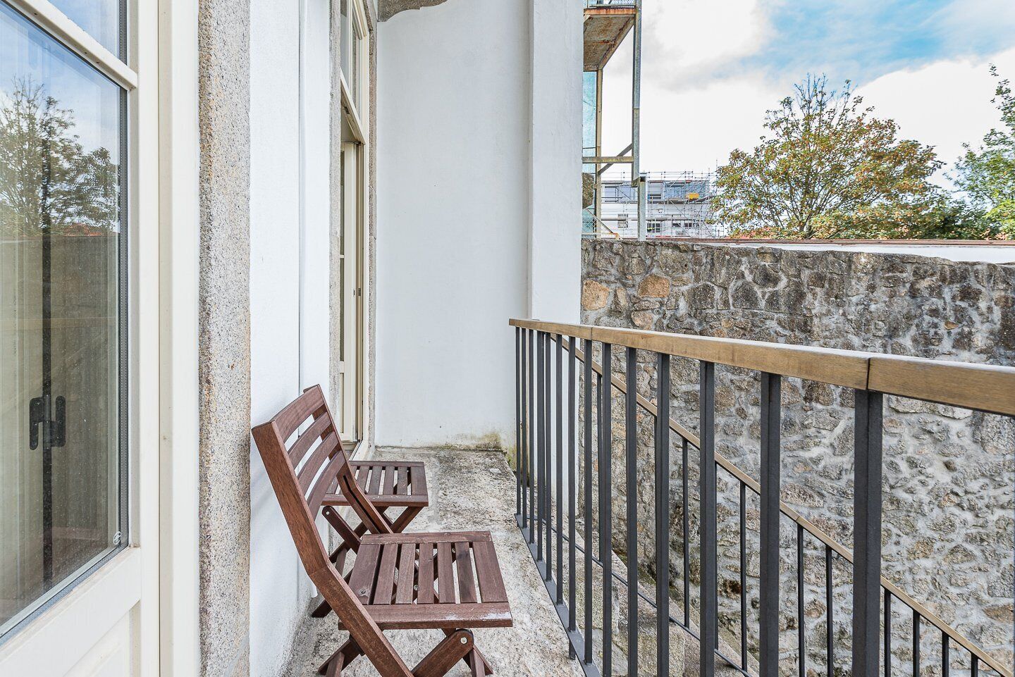 A balcony with two wooden chairs and a metal railing.
