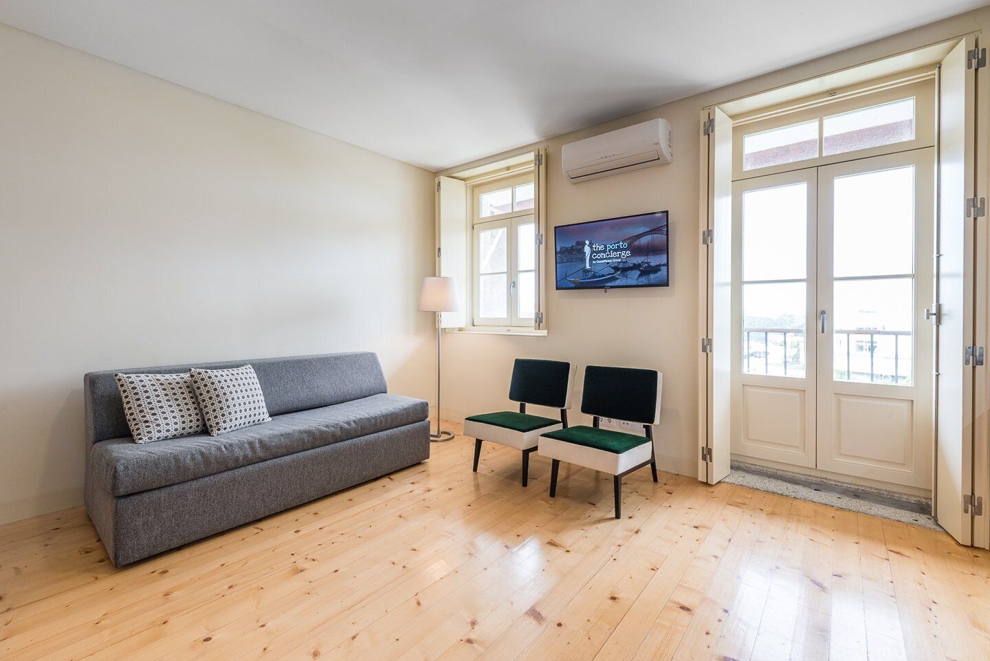 Ein modernes Wohnzimmer mit einem grauen Sofa, zwei grünen Sesseln, einem Flachbildfernseher und einem Fenster mit Blick.