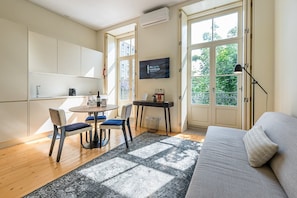 A modern living room with a sofa, a dining table with chairs, a TV, and a large window with a view of greenery. - Guestready - La Maison Aires Gouveia (Porto)