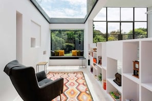 Un intérieur moderne agrémenté d’une lucarne, d’une chaise noire, d’un tapis à motifs, d’un banc avec des coussins et d’une bibliothèque.