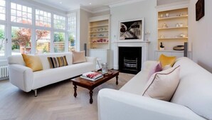 A spacious living room with a white sofa, a coffee table, and a fireplace. - Quartz House (Richmond upon Thames)
