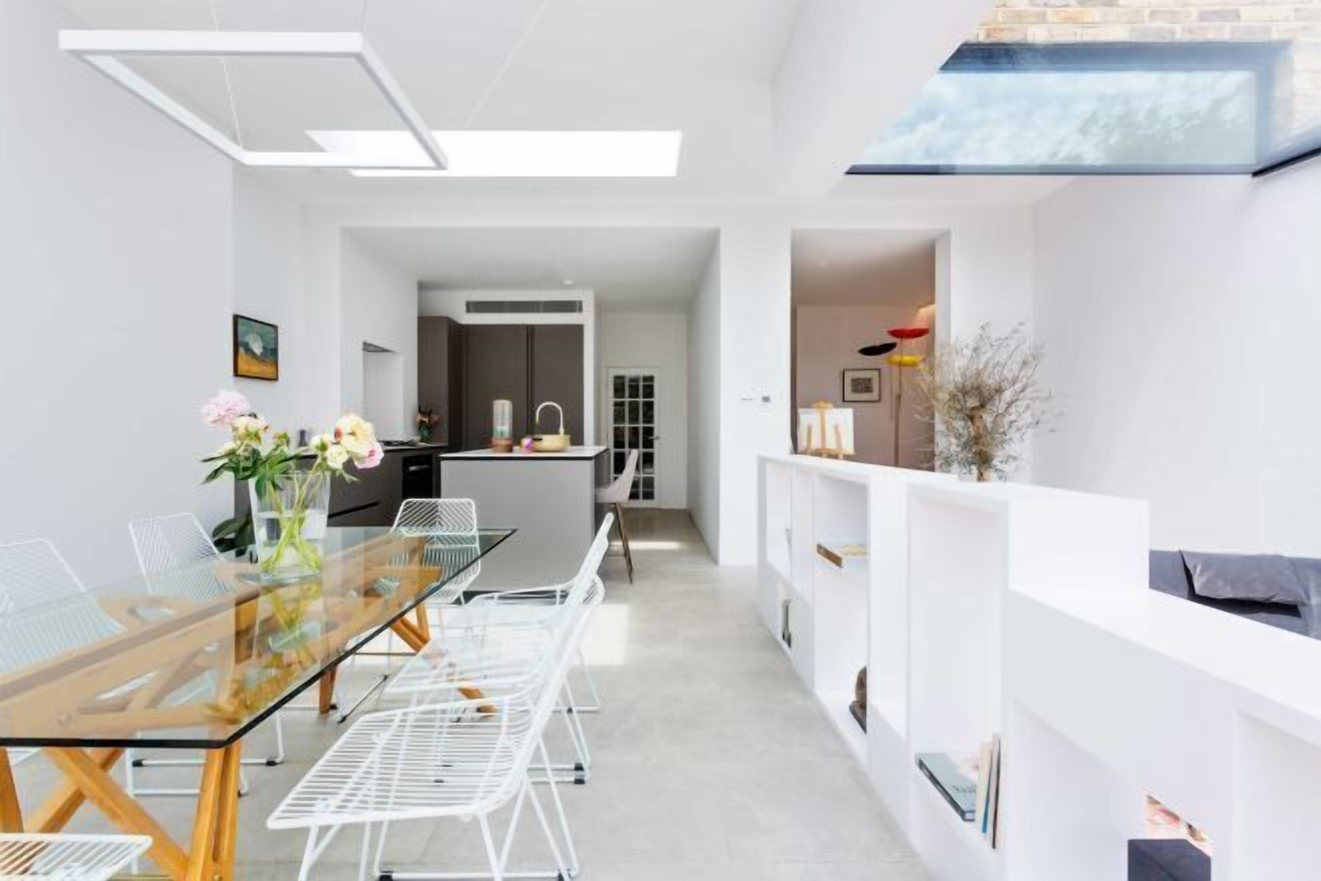 A modern kitchen with white cabinetry, a built-in oven, and a dining area with a glass table and white chairs.