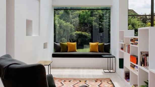 A modern room with a skylight, a window seat with cushions, a bookshelf, and a patterned rug. - Quartz House (Richmond upon Thames)