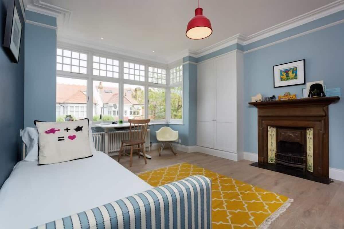A room with a bed, a desk, a chair, a fireplace, and a window.