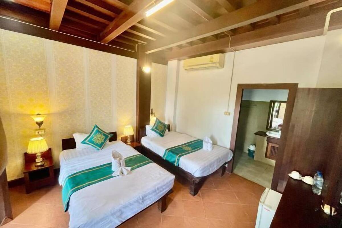 Une chambre d’hôtel avec deux lits, une table de chevet avec une lampe, un appareil de climatisation et un miroir.