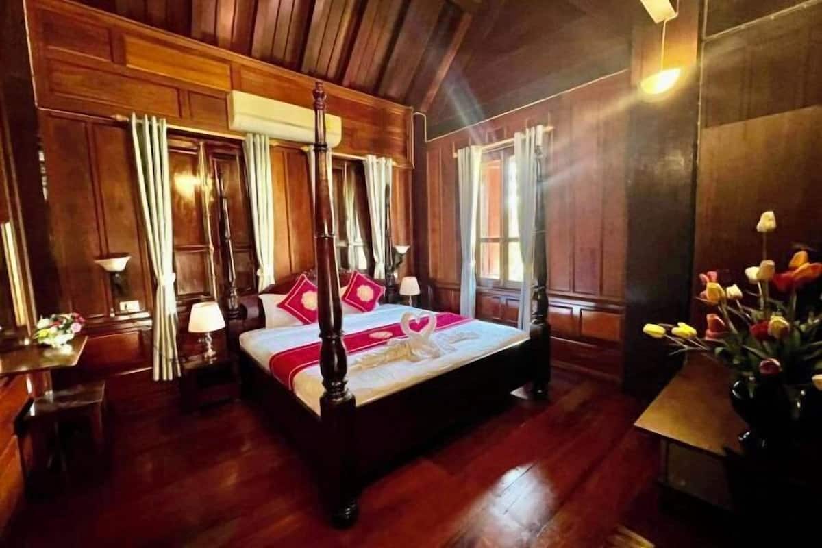 Un lit à baldaquin avec un couvre-lit blanc et des coussins rouges, un plancher en bois et un vase de tulipes posé sur une table d’appoint.