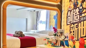 Hotellihuone, jossa on sänky, pieni pöytä, jossa on leluja, ja seinä, joka on koristeltu värikkäillä koriste-esineillä.