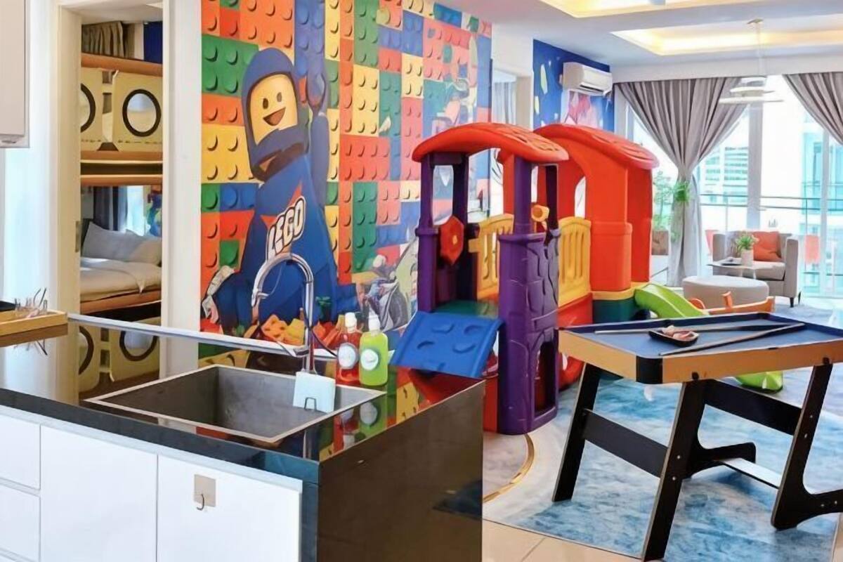 Uma área de recreação infantil com uma parede de LEGO, uma casinha e uma mesa de jantar.