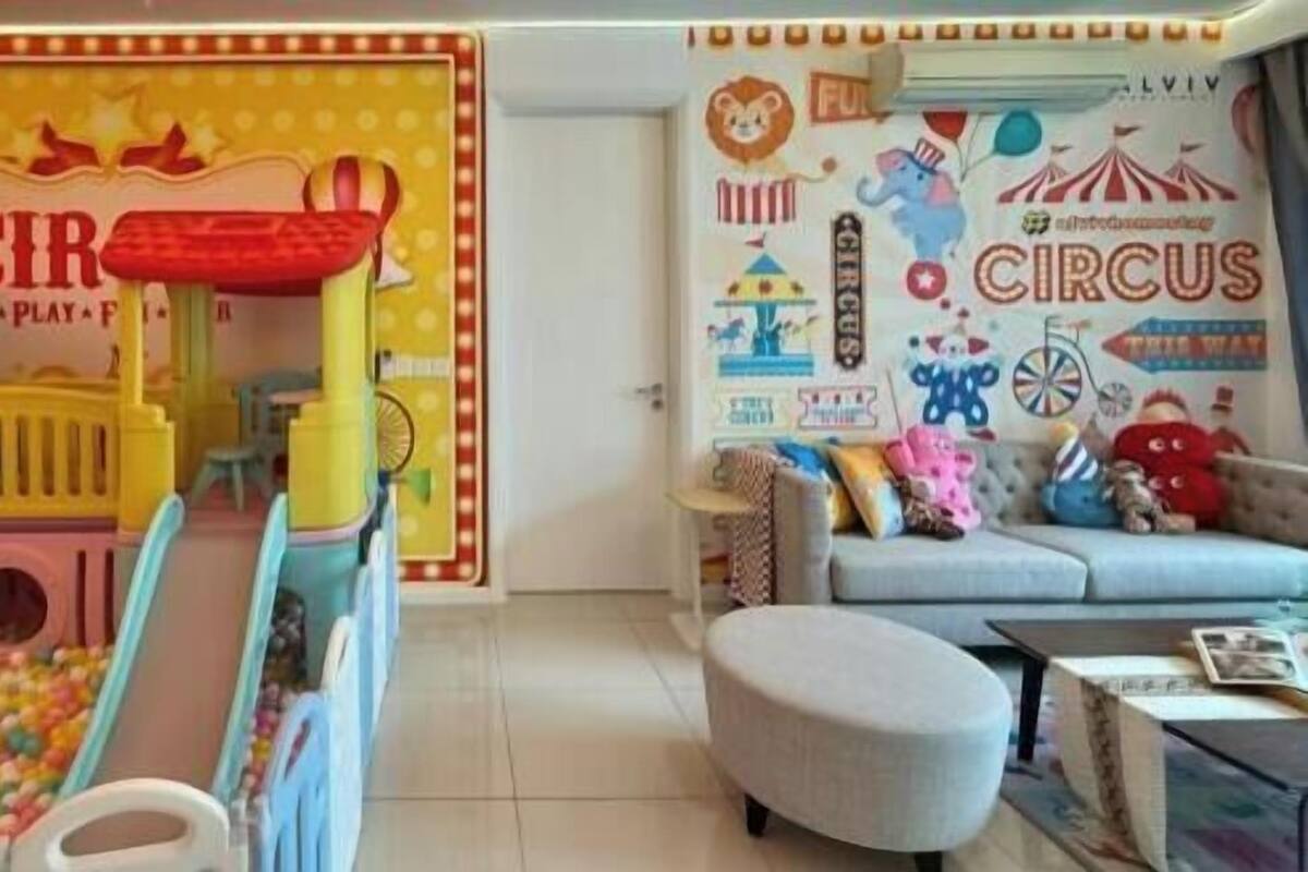 Uma área de recreação com escorrega e piscina de bolinhas, um sofá e uma parede decorada com tema de circo.