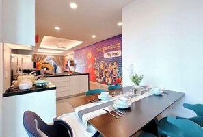 A modern dining area with a table set for four, a kitchen in the background, and a colorful mural advertising Lego play.