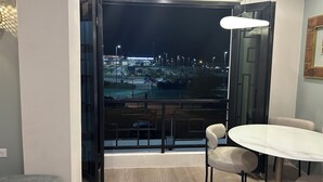 Una habitación moderna con un amplio ventanal que da a un paisaje urbano nocturno, una mesa redonda con sillas y una lámpara colgante.