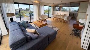 Ein modernes Wohnzimmer mit einer großen Eckcouch, einem Essbereich und Blick durch große Fenster.