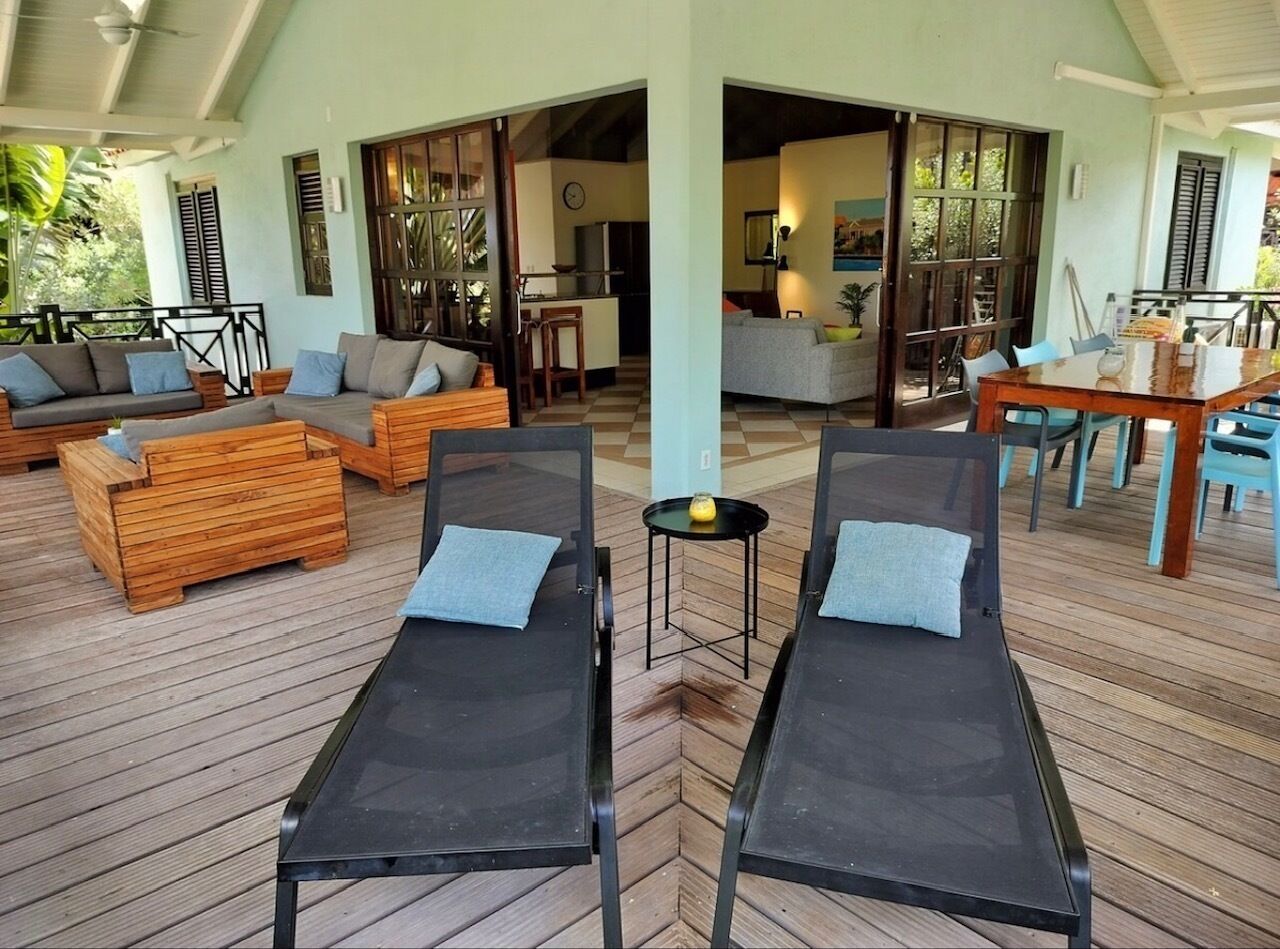 A covered outdoor area with two sun loungers, wooden furniture, and a dining table.