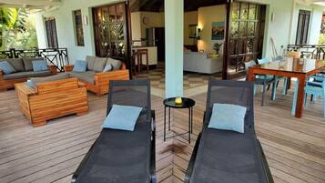 A covered outdoor area with two sun loungers, wooden furniture, and a dining table.