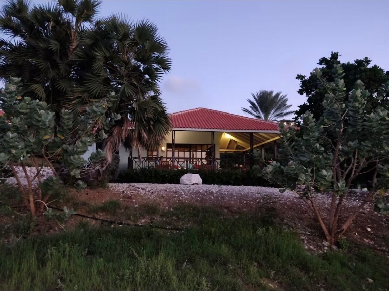 A building with a red roof, surrounded by palm trees and other vegetation.