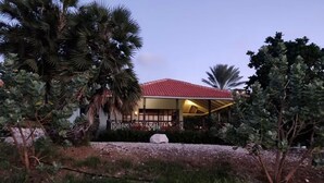 A building with a red roof, surrounded by palm trees and other vegetation. - Enjoy a spacious modern Villa, situated next to Golf Course and Pool and Beach (Sint Michiel)