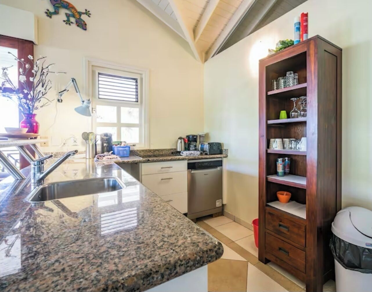 A kitchen with granite countertops, a dishwasher, a wooden cabinet, and a window with blinds.