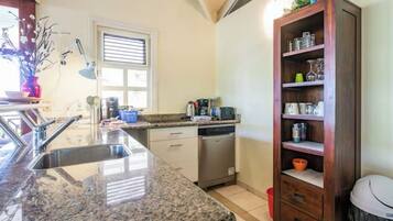 A kitchen with granite countertops, a dishwasher, a wooden cabinet, and a window with blinds.
