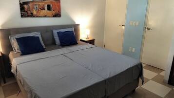 A bedroom with a bed, two nightstands, a lamp, a wall-mounted painting, and a door.