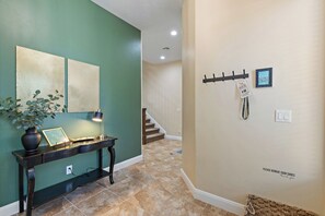 A hallway with a green wall, a console table with a vase and a framed picture, a wall-mounted key rack, and a 'Please remove your shoes' sign. - Pebble Beach Retreat (Washington)
