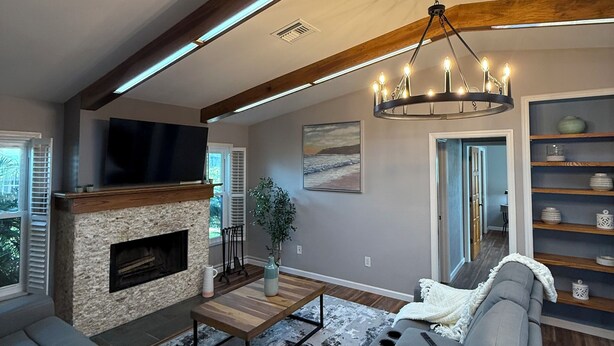 A modern living room with a fireplace, a large sofa, a coffee table, and a chandelier. - Pelican’s Cove, Gulf Access, Pool, & Dock (Cape Coral)