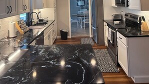 A modern kitchen with black marble countertops, white cabinetry, and pendant lighting. - Pelican’s Cove, Gulf Access, Pool, & Dock (Cape Coral)