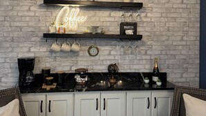 A modern kitchen with a brick wall, a neon coffee sign, a coffee maker, and a wine bottle. - Pelican’s Cove, Gulf Access, Pool, & Dock (Cape Coral)